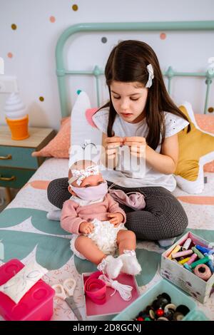 Girl sewing face masks for herself and her baby doll Stock Photo