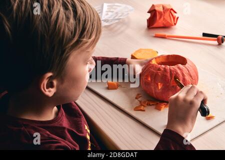 Halloween, decoration and holidays ideas- close up of kid with knife carving pumpkin or jack-o-lantern. 6 years boy has homefamily fun activity. Mom Stock Photo