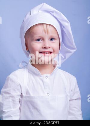 a 3-year-old boy in a suit and a chef's cap smiles at the camera. little chef Stock Photo