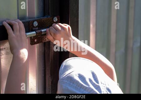 Close-up of boy's hand open the iron gate, the child runs away from adults, Boy locking the door Stock Photo