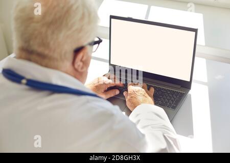 Senior man sitting in a bright room behind a laptop and typing on the keyboard. Close up. Stock Photo