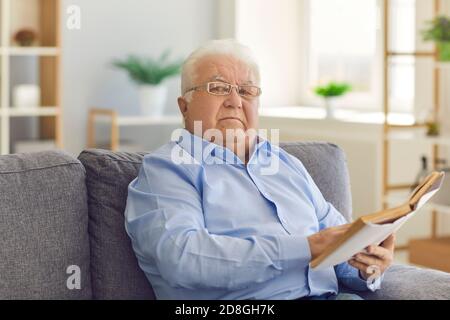 Portrait of a serious focused senior man sitting on the couch and reading an interesting book. Stock Photo