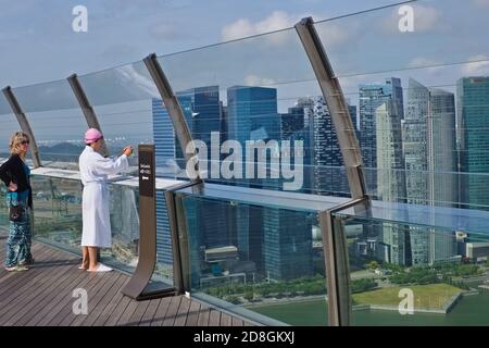 A guest of Marina Bay Sands Hotel in bath robe and up on the hotel's roof, the SkyPark, takes photos of the Singapore skyline; Marina Bay Singapore Stock Photo