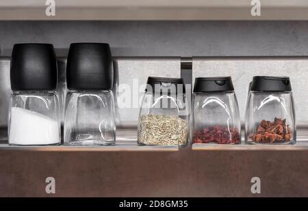 Glass jars with various spices and seasonings on the kitchen shelf. Stock Photo