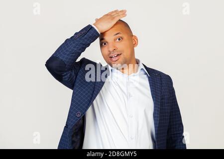 Portrait of surprised young african american businessman guy, resting hand on head for mistake, remember mistake Forgotten, bad memory concept. Standing on a gray background Stock Photo