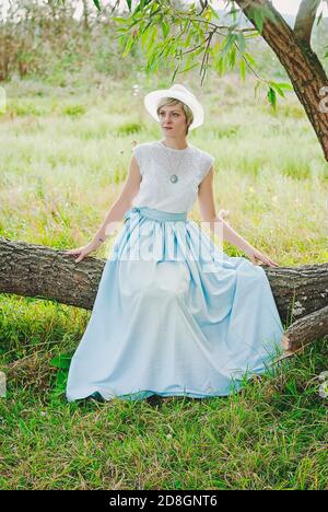 Young elegant happy lady with hat in vintage clothes walking alone in the nature in green field. Stock Photo