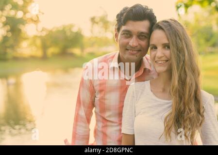 Close up of happy multi ethnic couple smiling and in love against scenic view of the lake in peaceful green park Stock Photo