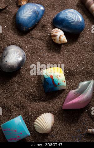 Overhead view of chocolate candies and seashells on brown sand Stock Photo