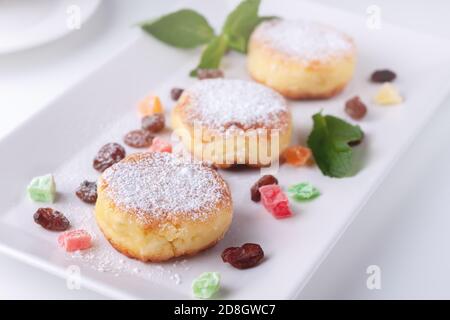 Curd pancakes with raisins and candied fruits on a white plate, top view
