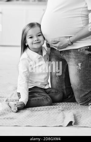 A portrait of a little daughter with her pregnant mother in the kitchen on a brick background with a blurred lights Stock Photo