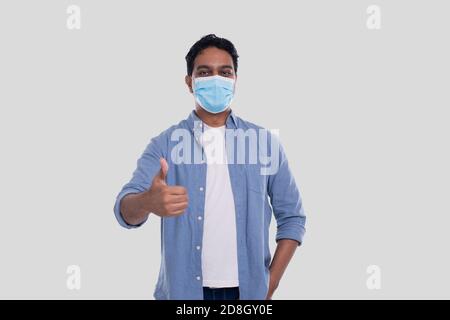 Indian Man Wearing Medical Mask Showing Thumb up Isolated. Man In Blue Shirt with Medical Mask. Health, Virus, Medical Concept Stock Photo