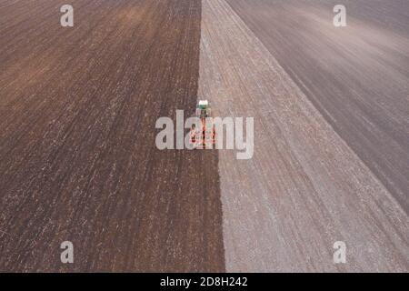 Lajoskomarom, Hungary - Aerial view of red tractor cultivating field at countryside after harvest. Farm concept, agricultural works at farmlands. Stock Photo