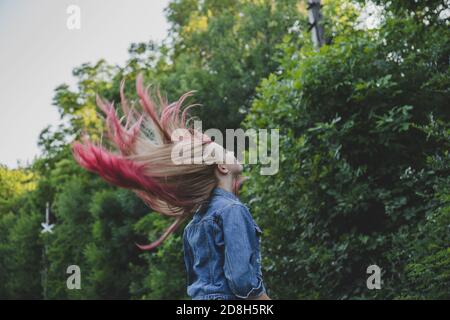 Flying long hair blonde girl in nature. The hair is blonde with pink dyed tips. Summer and green plants. Stock Photo