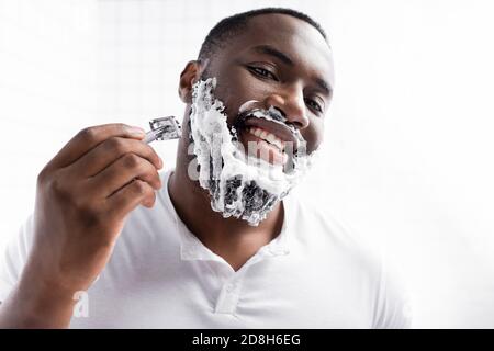 portrait of happy afro-american man shaving beard with razor Stock Photo