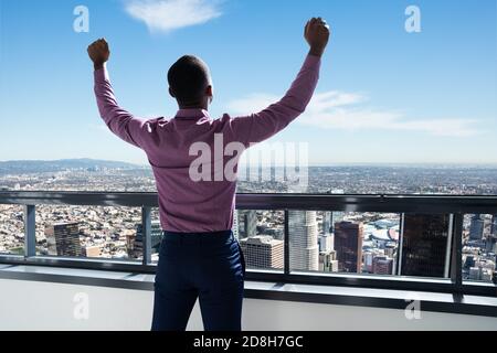 African Businessman Raising Hands. Rear View Near Window With City Downtown Stock Photo