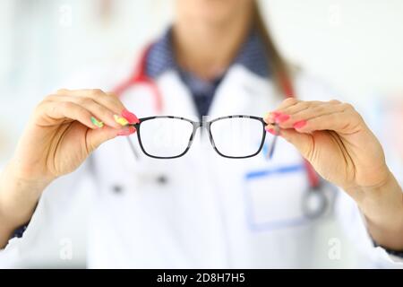 Ophthalmologist with stethoscope around neck holds glasses for vision in clinic closeup Stock Photo