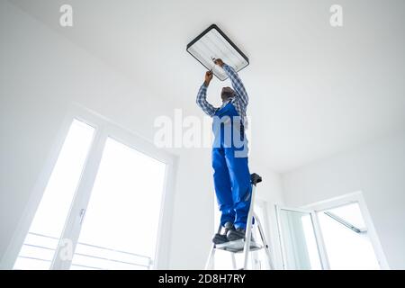 African Maintenance Electrician On Ladder Fixing And Installing Light Stock Photo