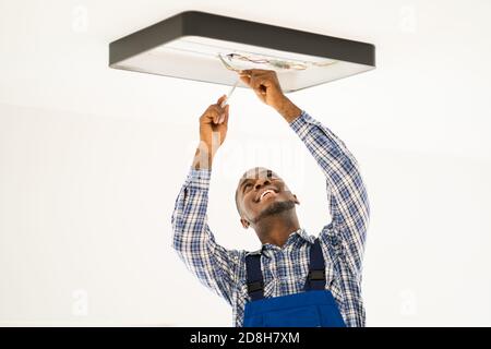 African Maintenance Electrician On Ladder Fixing And Installing Light Stock Photo