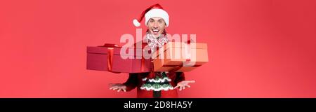 Cheerful man in santa hat throwing presents on red background, banner Stock Photo