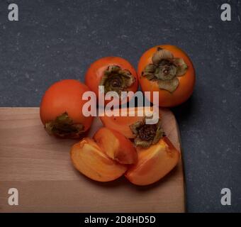 Kaki, autumn fruits, whole and pieces, on a wooden and stone base Stock Photo