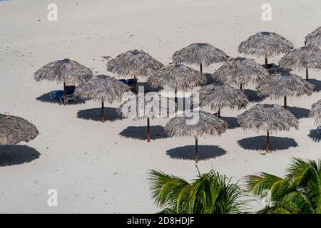 A lot of straw umbrellas standing in a row and sun loungers stand on the white sand against a blue cloudy sky. Varadero, Matanzas Province, Cuba Stock Photo