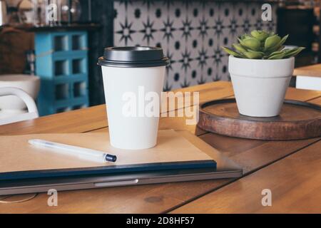 Laptop, notebook, pen hot drink tea or coffee on table in cafe. Distance learning or work concept Stock Photo