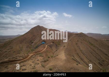 A bright blue painted water reservoir and pumping station can be seen atop a dry and barren hill on the island of Maio in Cape Verde. Stock Photo