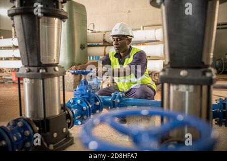 A professional male worker operates a new equipment valve at a water reservoir and pumping station on Maio Island, Cabo Verde. Stock Photo