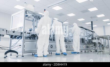 In the Manufacturing Facility Team of Scientist Wearing Sterile Protective Coverall Set's up Programs Modern Industrial 3D Printer, High Precision Stock Photo