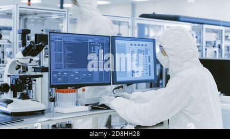 In Laboratory Over the Shoulder View of Scientist in Protective Clothes Doing Research on a Personal Computer. Modern Manufactory Producing Stock Photo
