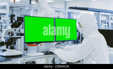 In Laboratory Over the Shoulder View of Scientist in Protective Clothes Working on Personal Computer with Green Screen Chroma Key Template Great for Stock Photo