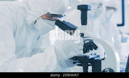 Close-up Shot of a Scientists in Protective Clothes Doing Research, Using Microscope In Laboratory. Modern Manufactory Producing Semiconductors and Stock Photo