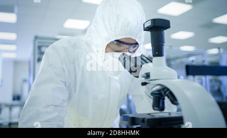 In Laboratory Scientist in Protective Clothes Doing Research Uses Microscope. Modern Manufactory Producing Semiconductors and Pharmaceutical Items. Stock Photo