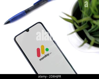 Lod, Israel - July 8, 2020: Modern minimalist office workspace with black mobile smartphone with Monday app launch screen with logo on white backgroun Stock Photo