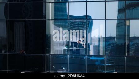 Aerial Shot From Outside of the Skyscraper: Businessman and Businesswoman Talking Business while Sitting at the Desk by the Office Window. Shot of the Stock Photo