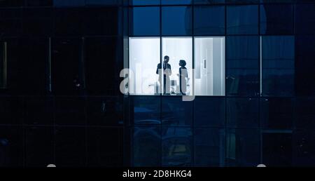 Aerial Shot From Outside of the Skyscraper: Businessman and Businesswoman Talking while Standing in the Office Window. Shot of the Business District Stock Photo