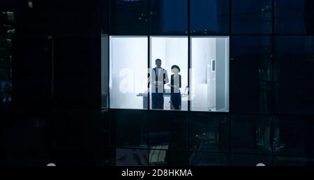 Aerial Shot From Outside of the Skyscraper: Businessman and Businesswoman Talking while Looking Out of the Office Window. Shot of the Business Stock Photo