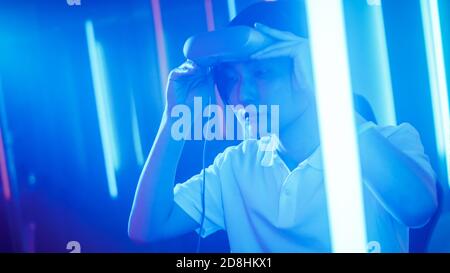 East Asian Pro Gamer Putting on Virtual Reality Headset and Plays Online Video Game with Joysticks Controllers. Cool Retro Neon Colors in the Room. Stock Photo