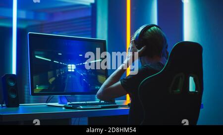 Pro Gamer Plays in the First Person Shooter on His Personal Computer. He Puts on His Headphones. Neon Colored Room. Online eSport Tournament in Action Stock Photo
