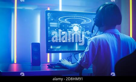 Arc Shot of the Professional Gamer Playing in First-Person Shooter Online Video Game on His Personal Computer. He's Talking with His Team Through Stock Photo