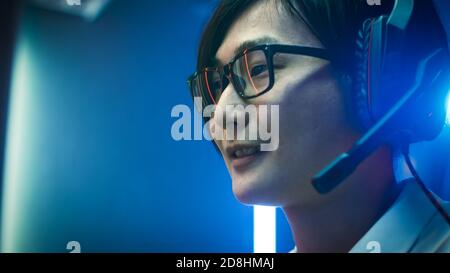 Close-up Portrait of the Professional Asian Gamer Playing in Online Video Game, He's wearing Glasses, talks chats with His Teammates Friends through Stock Photo