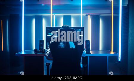 Professional Gamer Playing in First-Person Shooter Online Video Game on His Personal Computer. Room Lit by Neon Lights in Retro Arcade Style. Cyber Stock Photo