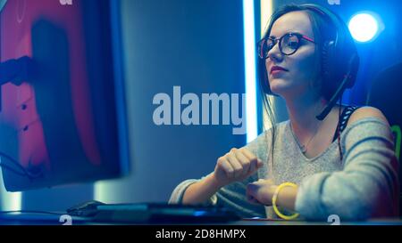 Beautiful Professional Gamer Girl Playing in Video Game on Her Personal Computer. Casual Cute Geek wearing Glasses, Streaming and Waiting for Download Stock Photo