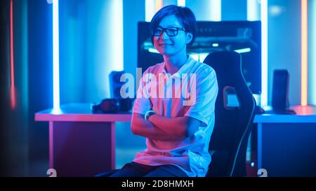 Shot of the Professional Gamer Sitting on His Gaming Chair and Smiling into Camera. Personal Computer. Room Lit by Neon Lights in Retro Arcade Style Stock Photo