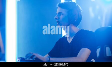 Shot of the Pro Gamer Playing in Video Games on His Personal Computer. Talking with His Team through Microphone on Headphones. Retro Neon Room. Stock Photo