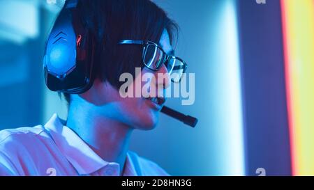 Low Angle Shot of the East Asian Pro Gamer Talking into Microphone on His Headsphones. Playing with Friends or Team in Championship. Stock Photo