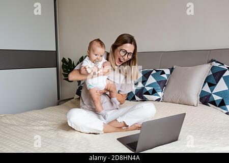 Telecommuting in quarantine. Mother showing baby to friends at the video chat. Stylish young freelancer working from home. Social distancing during Stock Photo