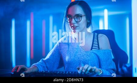 Beautiful Professional Gamer Girl Playing and Streaming Online Video Game on Her Personal Computer. Casual Cute Geek wearing Glasses. Cyber e-Sport Stock Photo