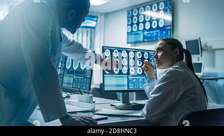 Two Scientists in the Brain Research Laboratory work on a Project, Using Personal Computer with MRI Scans Show Brain Anomalies. Neuroscientists at Stock Photo