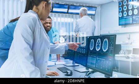 Diverse Team of Medical Scientists Solve Problems and Point at Computer Screens Showing CT, MRI Scans. Neurologists Neuroscientists Working in Brain Stock Photo